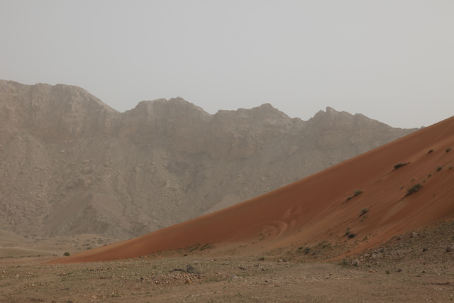 Red dunes meet the foothills of the Hajar Mountains
